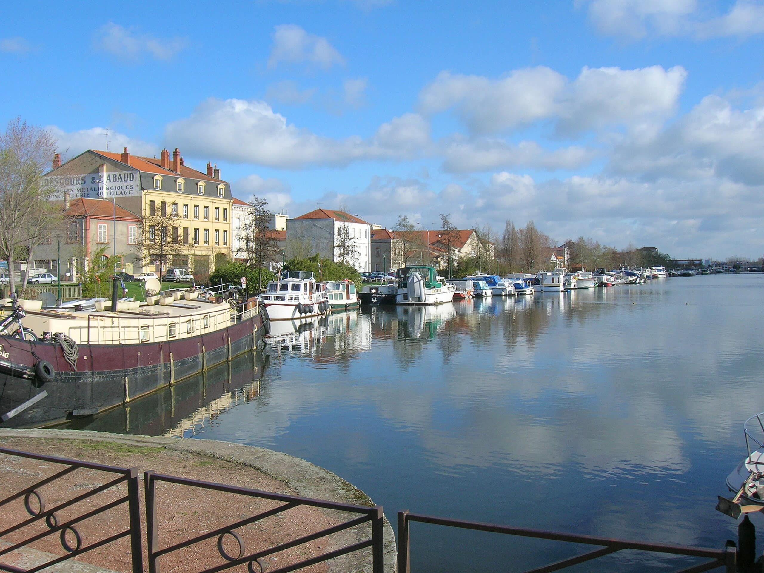 Vue panoramique Roanne, rivière calme, bateaux à quai, journée ensoleillée.